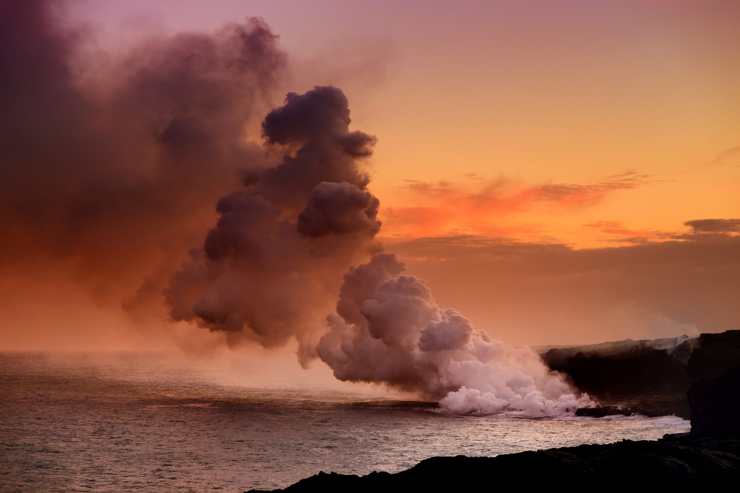 Volcanic steam rising at sunset ocean beach.